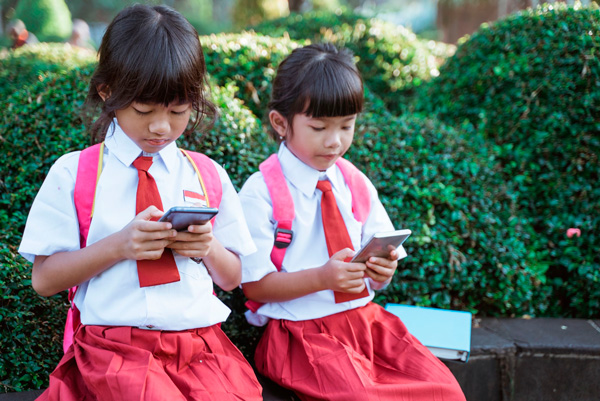 Duas crianças usando smartphones, representando o futuro do uso destas tecnologias.