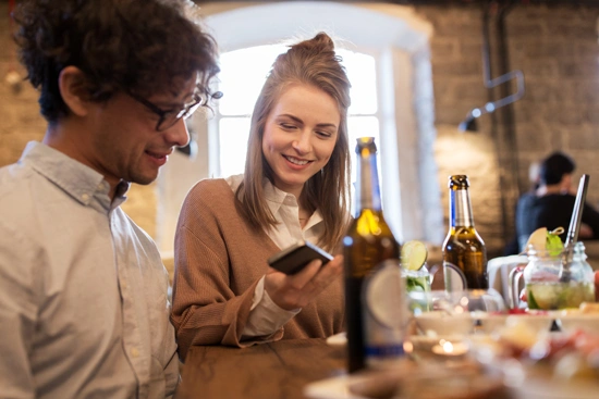 Pessoas usando smartphone em restaurante, realizando check-in, ferramenta do geomarketing.