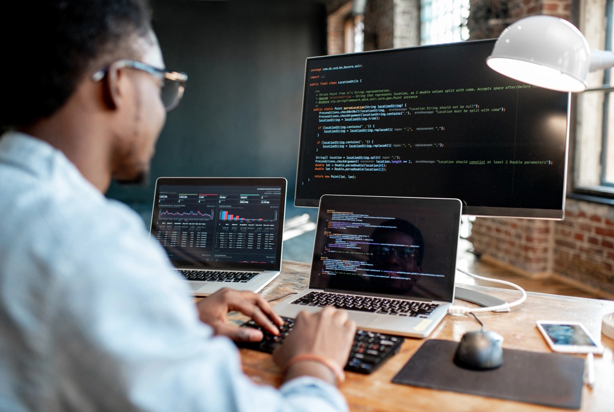 Programador trabalhando com frameworks de programação, em frente a três telas de código.